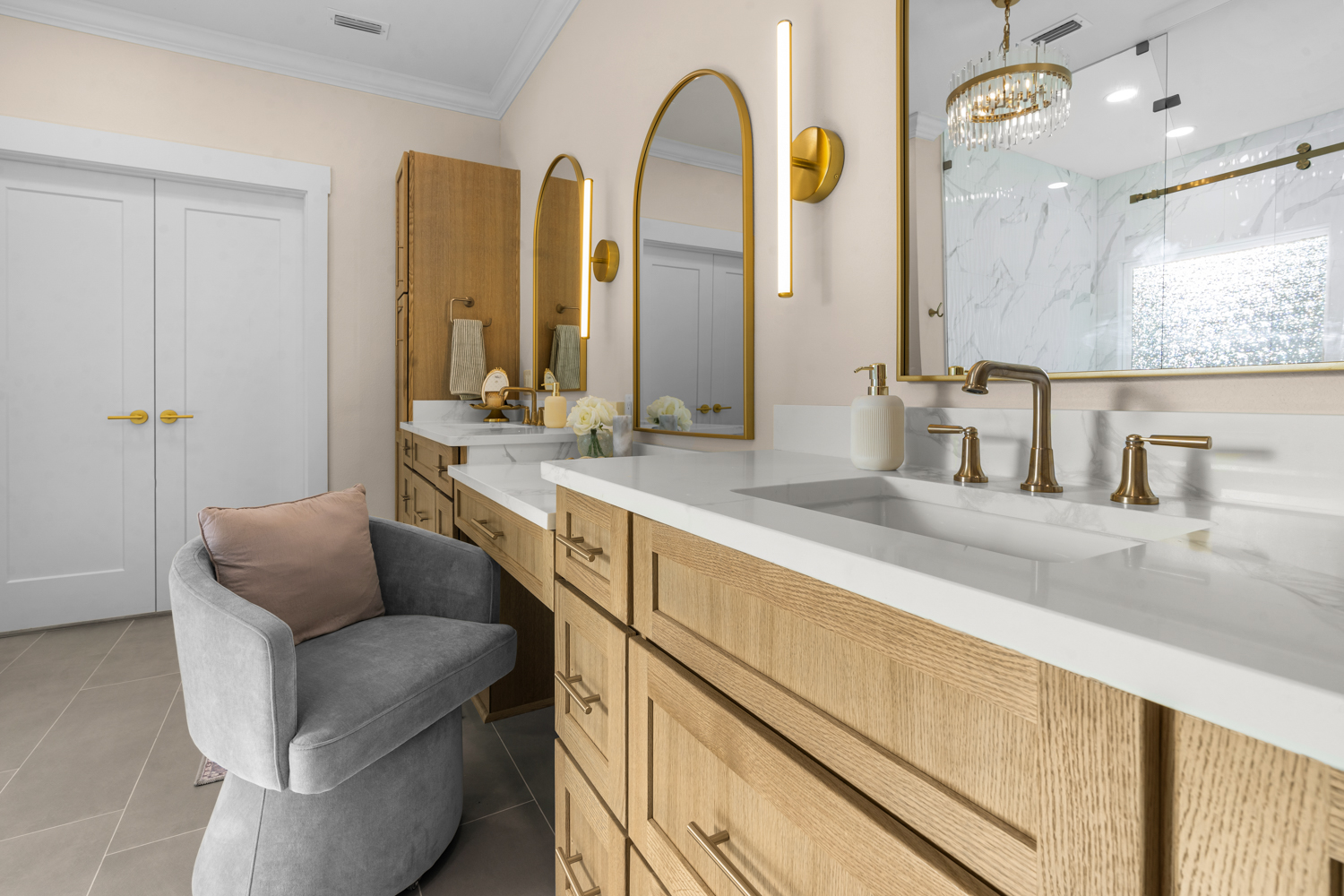 Oak double vanity with arched mirrors, brass sconces and a velvet stool