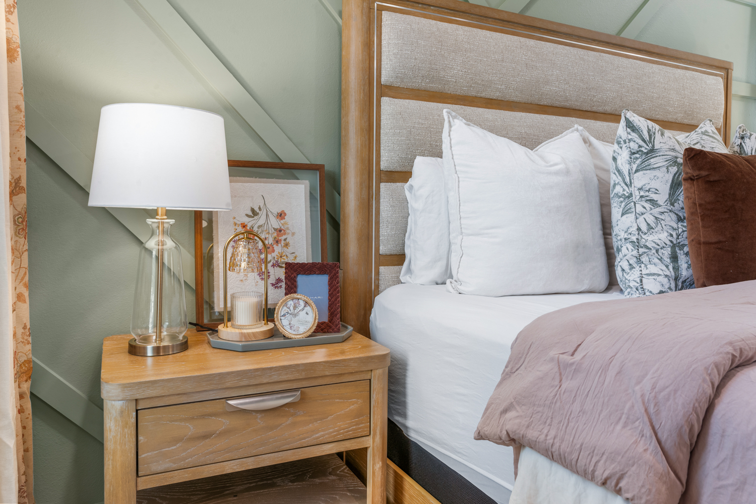 Bed dressed in white and blush linens against a sage paneled wall