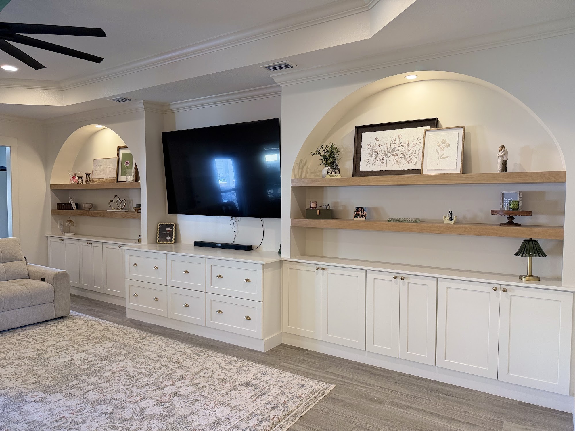 Living room with arched built-in shelving flanking a wall-mounted television above white cabinetry