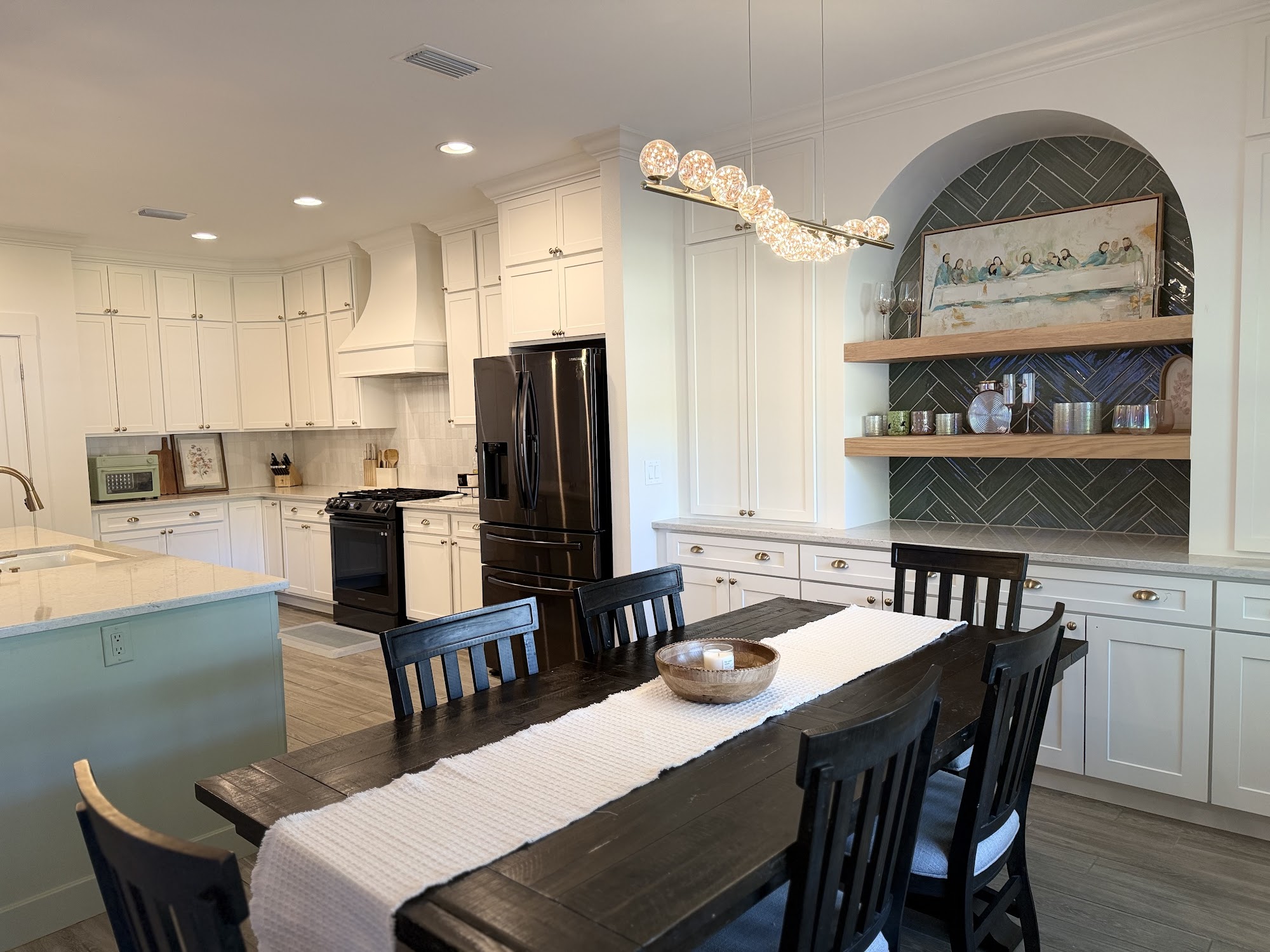 Kitchen and dining seen together, with a long island, pendant lighting and a curved timber feature above