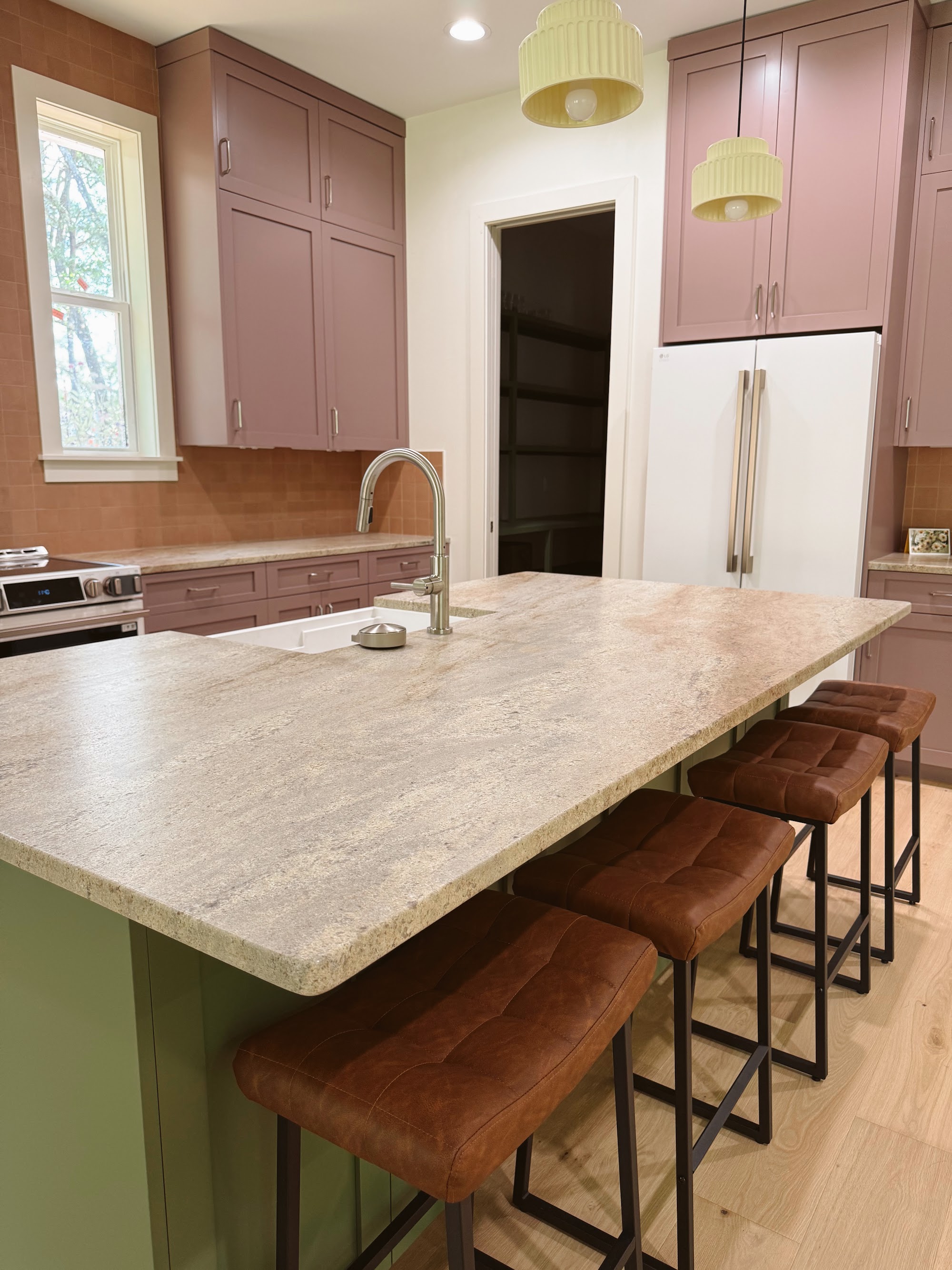 Kitchen in warm tones with a stone counter, timber stools and a range beyond