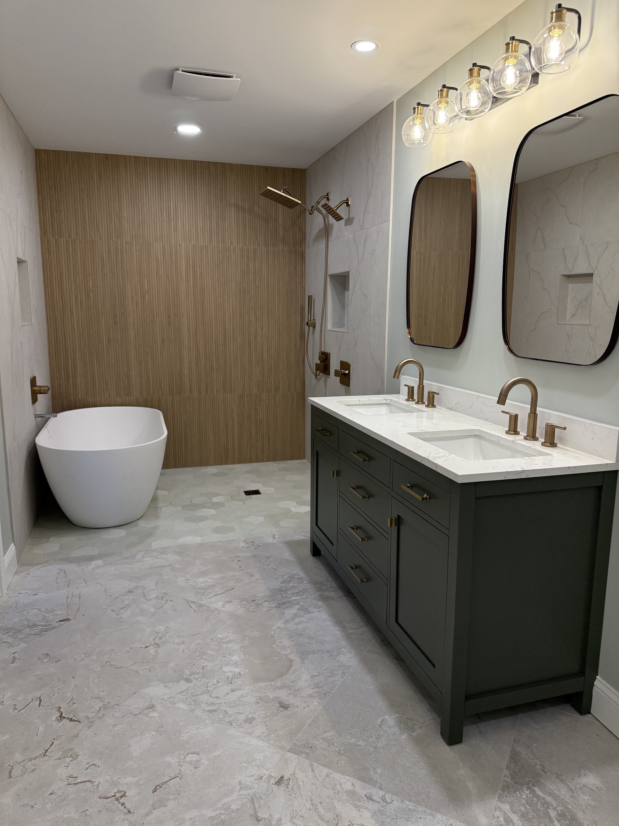 Freestanding tub beside a deep green double vanity with brass fixtures