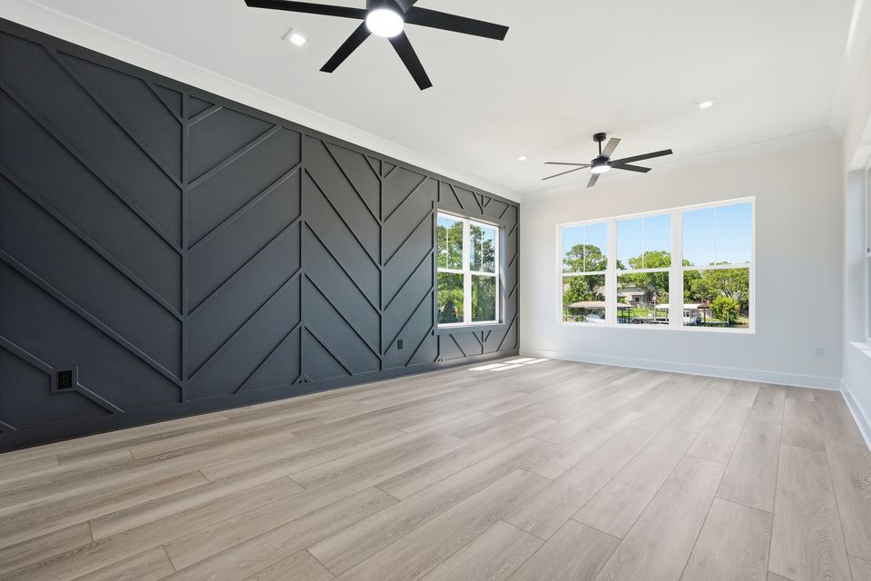 Primary bedroom with a dark chevron panelled feature wall, pale oak floor and windows on two sides