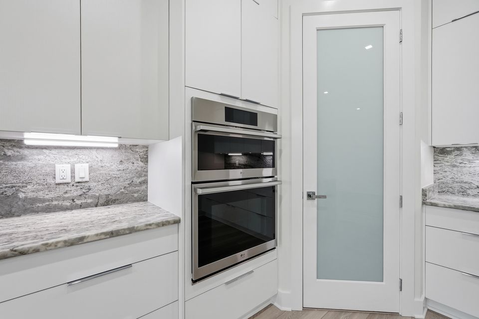 Built-in double ovens set into white cabinetry beside a glazed pantry door