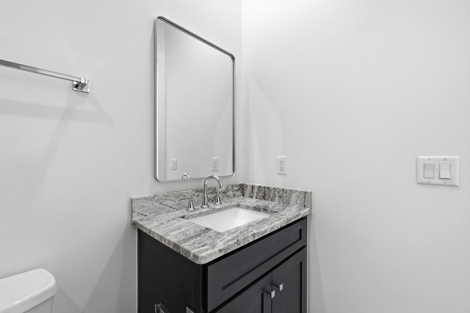 Single vanity in dark cabinetry with a stone top and a slim rounded mirror above
