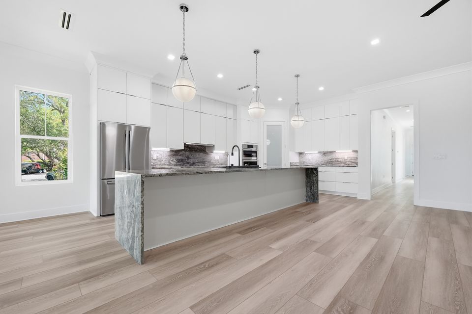 Kitchen island with a stone waterfall edge, pendant lighting above and integrated appliances beyond