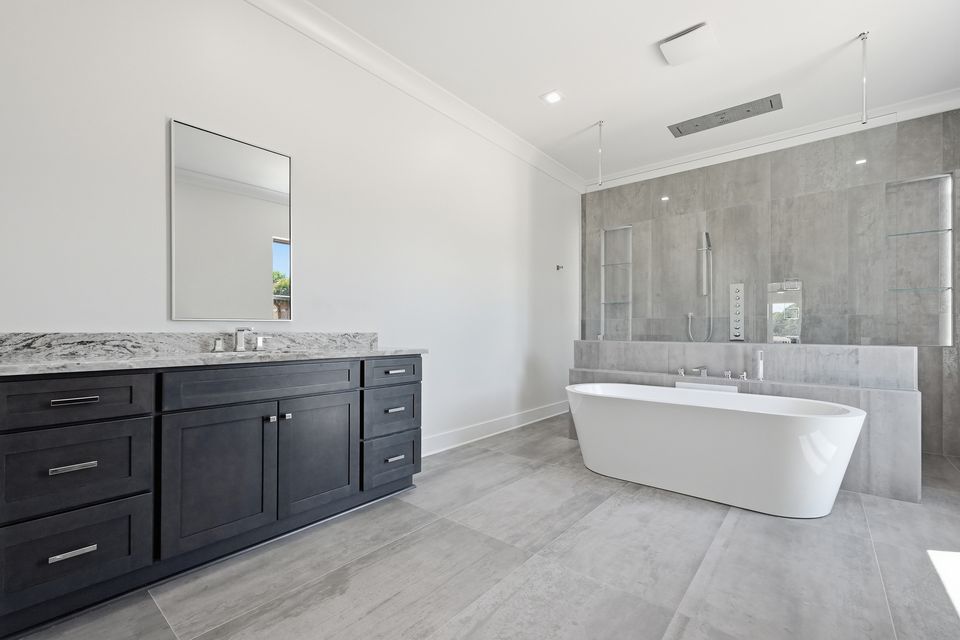 Primary bathroom with a dark double vanity, stone counter and a freestanding tub beyond
