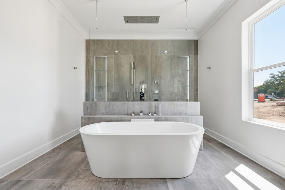 Freestanding soaking tub set against a stone-clad wall with a window alongside