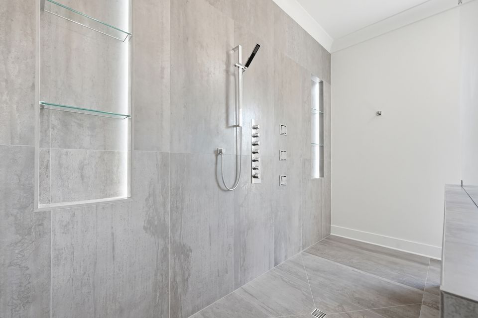Walk-in shower lined in large-format stone-look tile with multiple shower heads and a linear drain